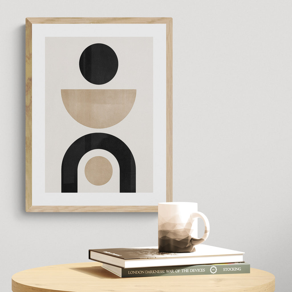 Framed abstract art print on a wall with books and a mug below.