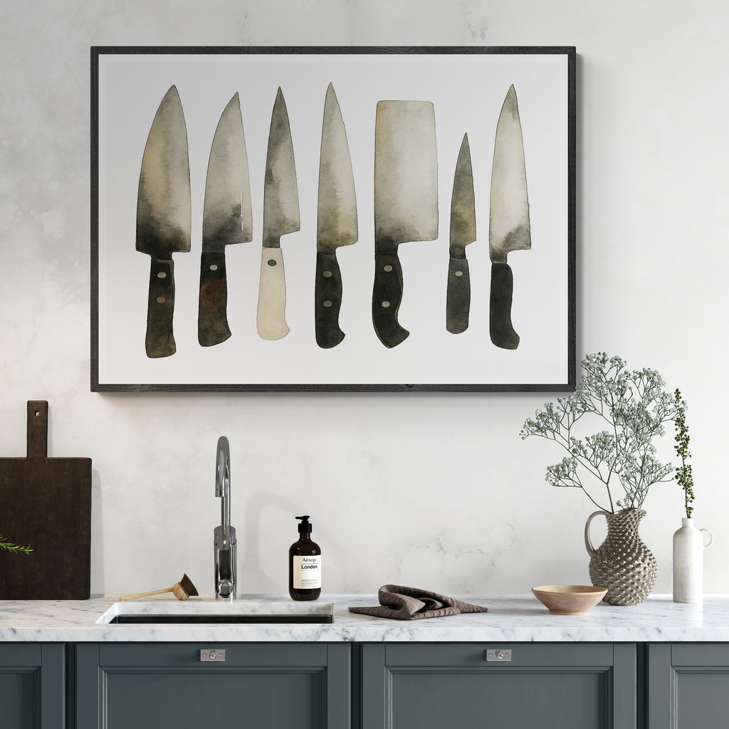 Framed artwork of knives on a kitchen wall with a sink and countertop.